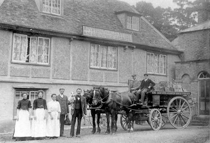 A delivery at the Coach and Horses pub, c. 1900. There is a horse-drawn cart from the Sawston Aerated Water Company in front of the pub and three women and two men, one holding a dog, in the foreground. Cambridgeshire Collection.