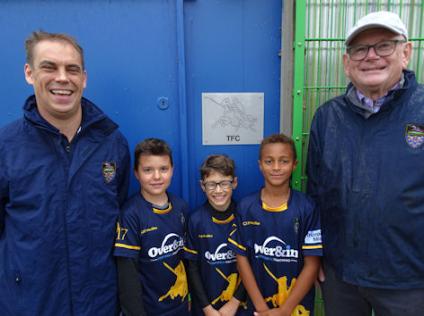 Ian Elston and Ed Davidson, two of the founder members of Trumpington Football Club, with three players from the Club, beside the TFC sign on the changing room, King George V Playing Field. Photo: Andrew Roberts, 12 October 2019.