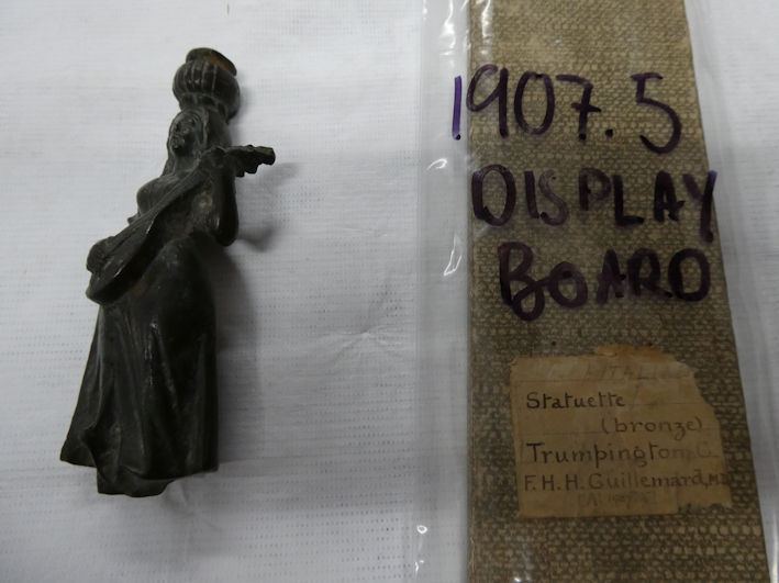 A copper alloy figure of a woman playing a mandolin balancing a pot or basket on her head, found in Trumpington (1907.5), the Centre for Material Culture. Photo: Andrew Roberts, 4 August 2026.