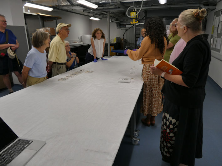 Rosie Croysdale talking to the group in the Cowles Workroom, with archaeological items found in Trumpington, the Centre for Material Culture. Photo: Andrew Roberts, 4 August 2026.