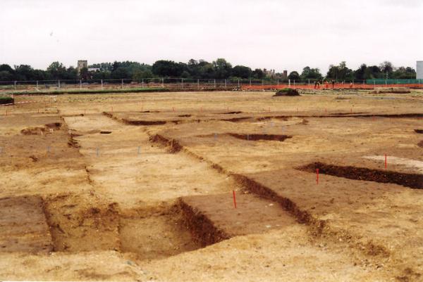 One of three Neolithic burial monuments being excavated on the Trumpington Meadows site (in the area of the future school playing field), with burials marked by white posts, burials in rectangular area, blue pegs marking earlier inner ring, red pegs outer ring with pottery dating from c. 3500BC, with Trumpington Church and Anstey hall in the distance. Photo: Andrew Roberts, 3 October 2010.