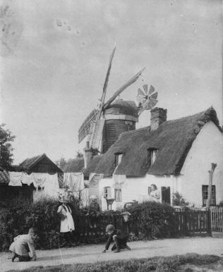 Windmill and thatched cottages near the junction of Long Road (Mill Road) and Trumpington Road, c. 1880. There is a path and cottages in the foreground, with a number of men, women and children and a line of washing, and the mill in the background. Photograph by R.H. Lord. Cambridgeshire Collection.